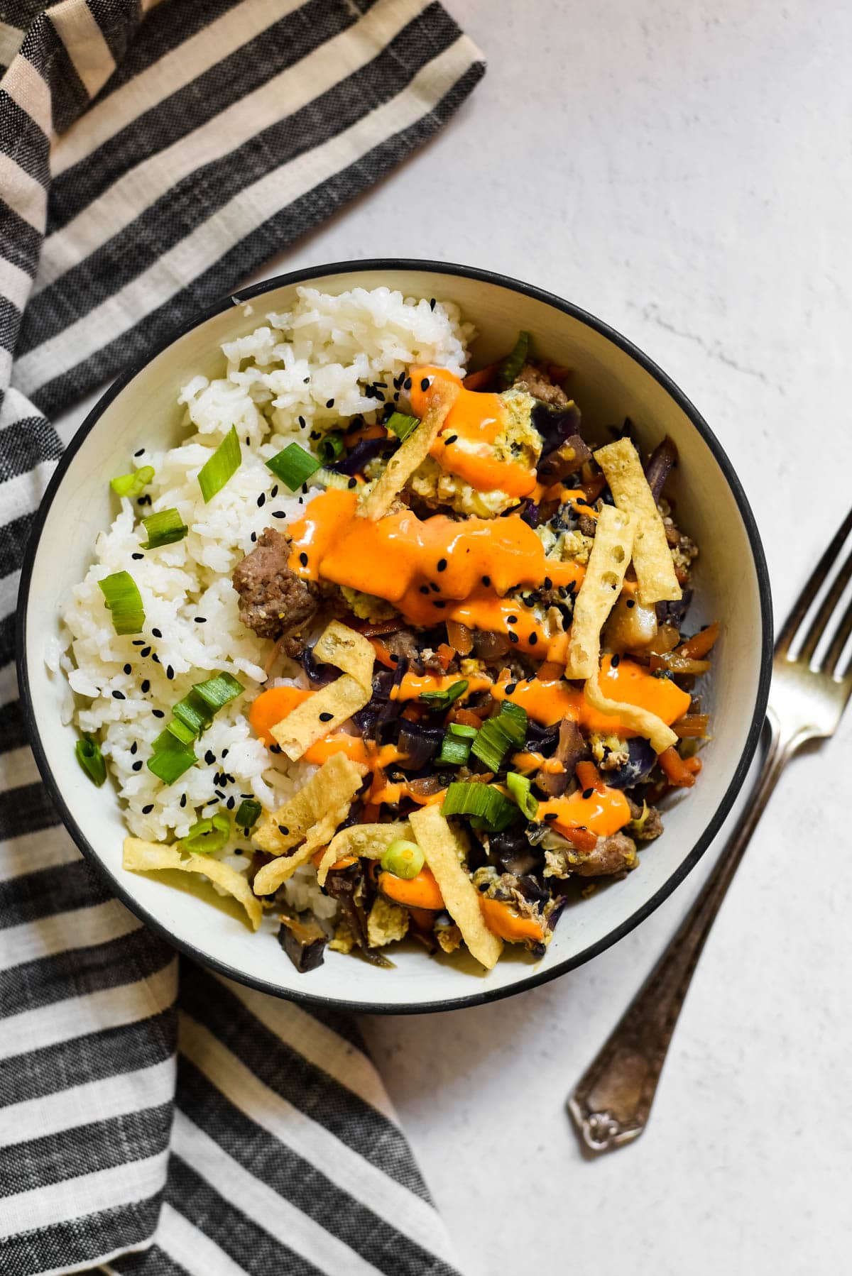 overhead view of egg roll in a bowl with fork and napkin on side