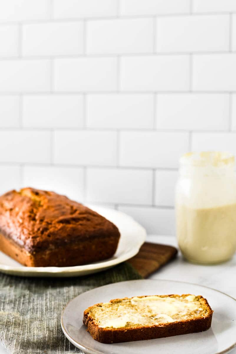 slice of banana bread with butter next to loaf and jar of sourdough stater