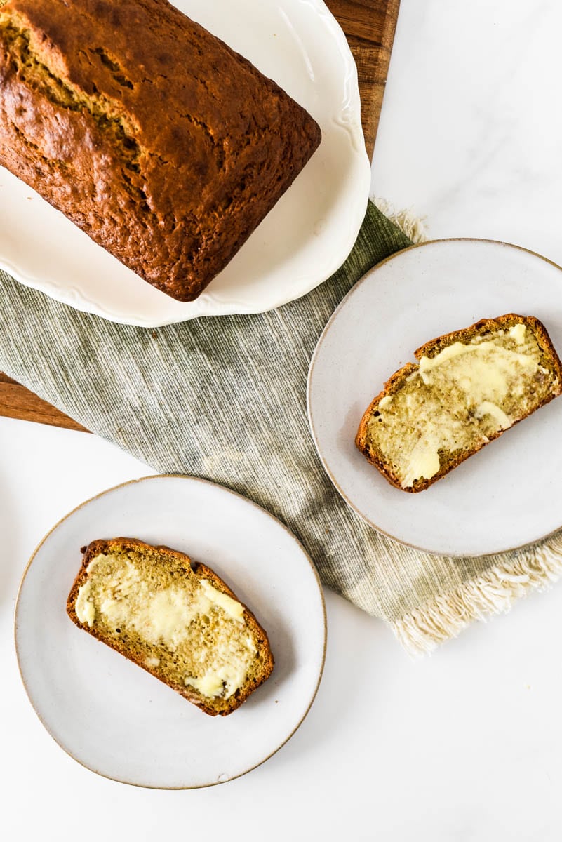 two plates with slices of sourdough banana bread smeared with butter, next to loaf