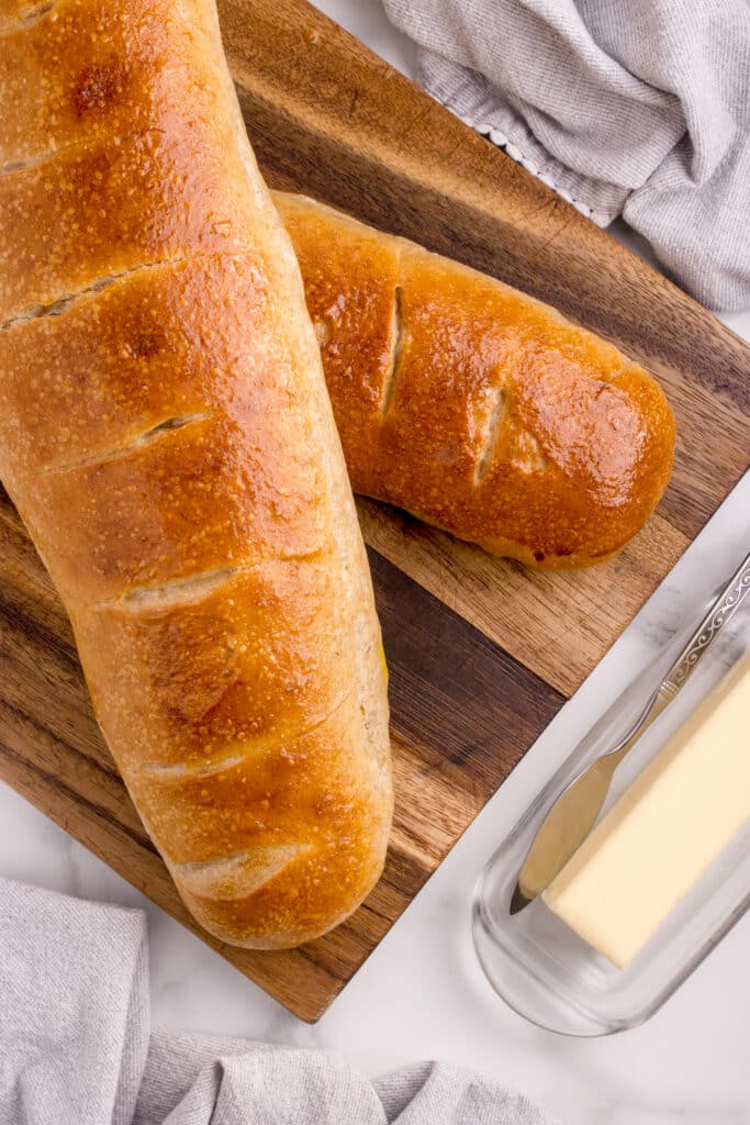 two loaves of french bread stacked at an angle next to butter