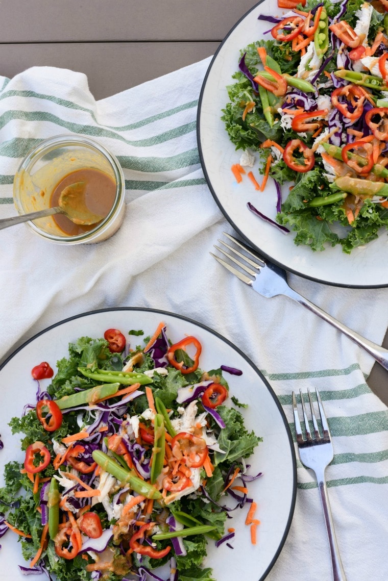 two thai chicken kale salad plates with forks and jar of dressing